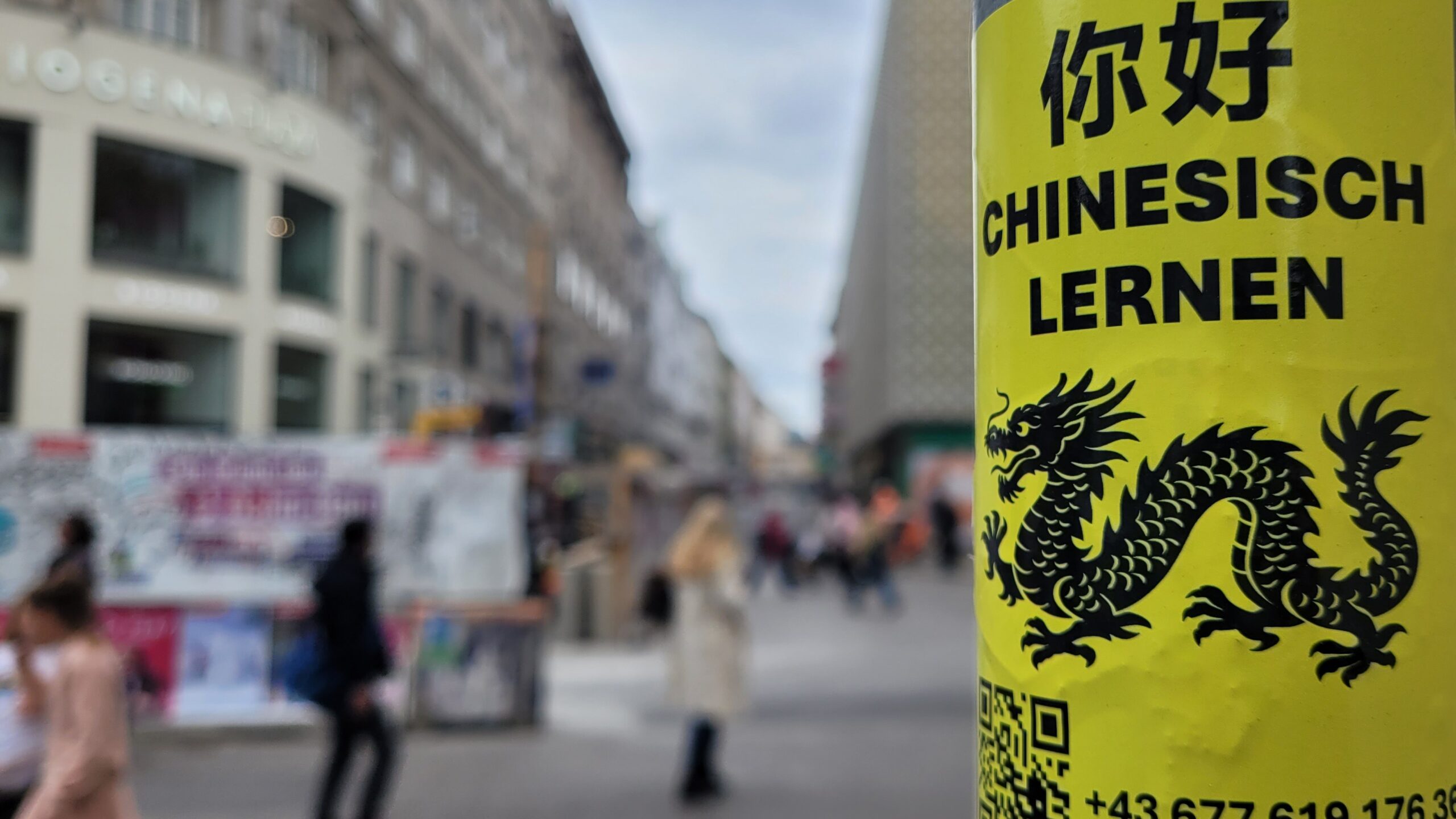 Ein Aufkleber mit der Aufschrift „Chinesisch Lernen“ klebt an einem Laternenpfahl.