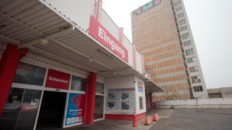 Der Eingang einer leerstehenden Baumarktfiliale der insolventen Firma Quester ist zu sehen, im Hintergrund ragt ein leerstehender Büroturm in die Höhe.