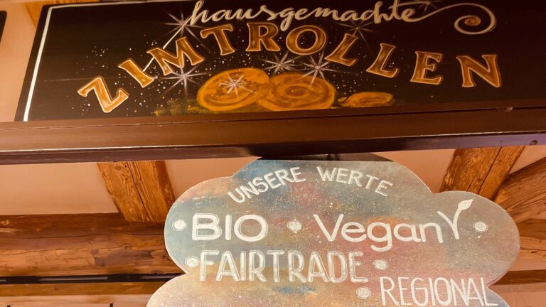Das Bild zeigt ein Schild mit der Aufschrift „hausgemachte Zimtrollen.“ Darunter werden die Werte des Standes aufgelistet: Bio, vegan, Fairtrade und regional.
