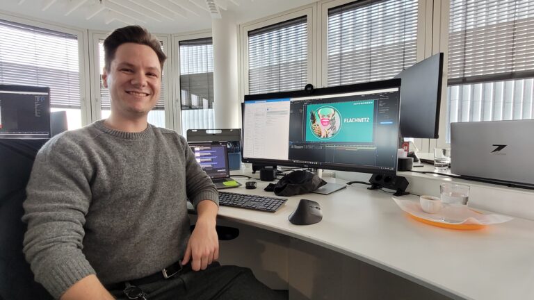 Benedikt Pilz sitzt an seinem Schreibtisch und lacht in die Kamera.