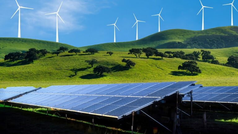 Ein Stromzähler im Vordergrund montiert an einer Wand, im Hintergrund Solarpanele und Windräder in einem grünen idyllischen Feld.