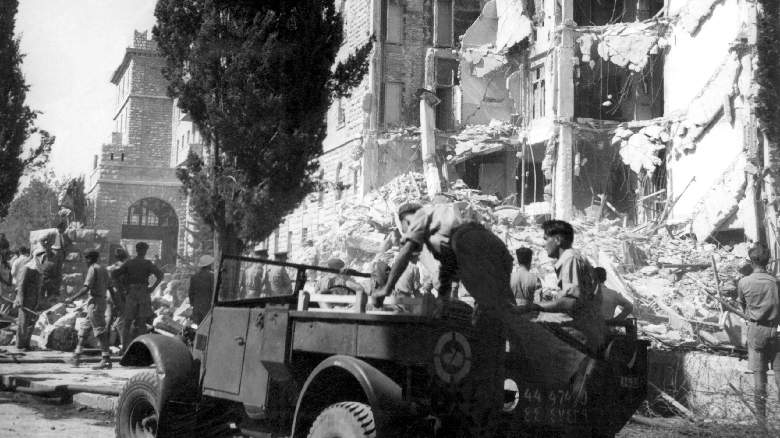 Schwarz-Weiß-Aufnahme eines Militärjeeps vor dem zerstörten Trakt des Hotels.