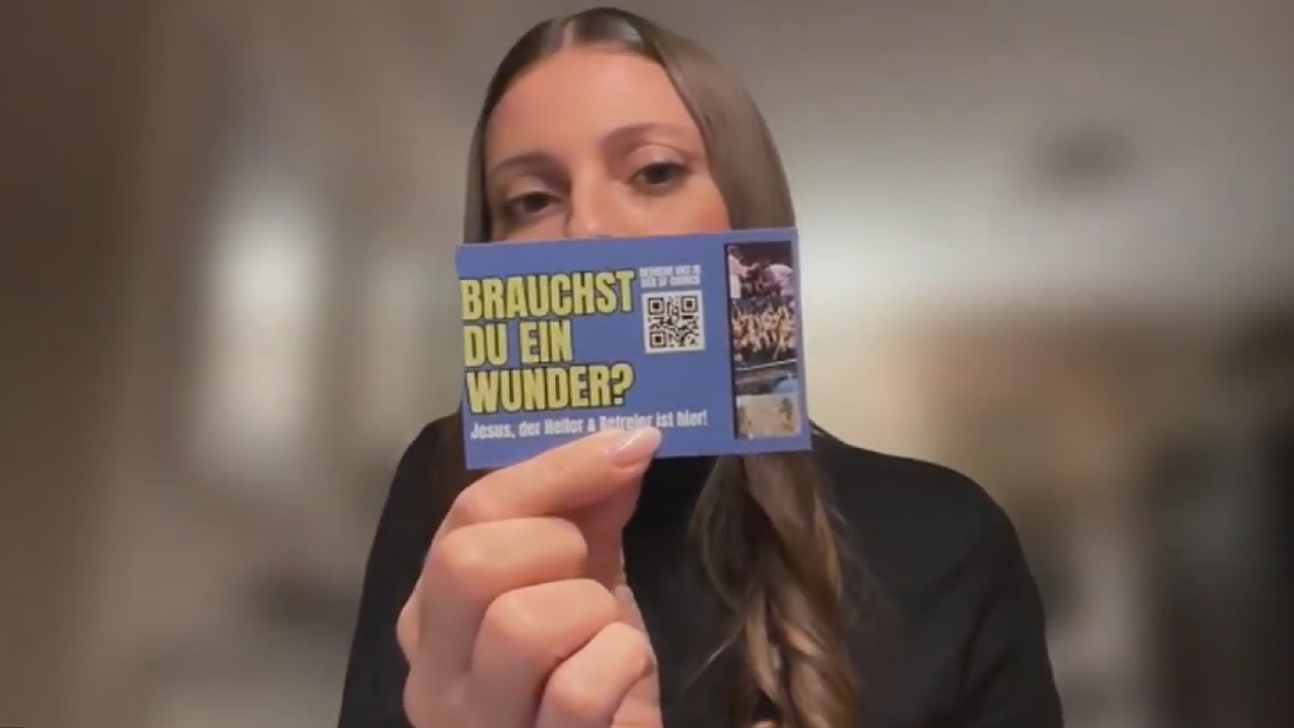 Vanessa hält eine Visitenkarte in die Kamera mit der Aufschrift "Brauchst du ein Wunder?"