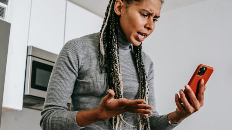 Eine Frau schaut aufgebracht auf ihr Smartphone, das sie in der Hand hält.