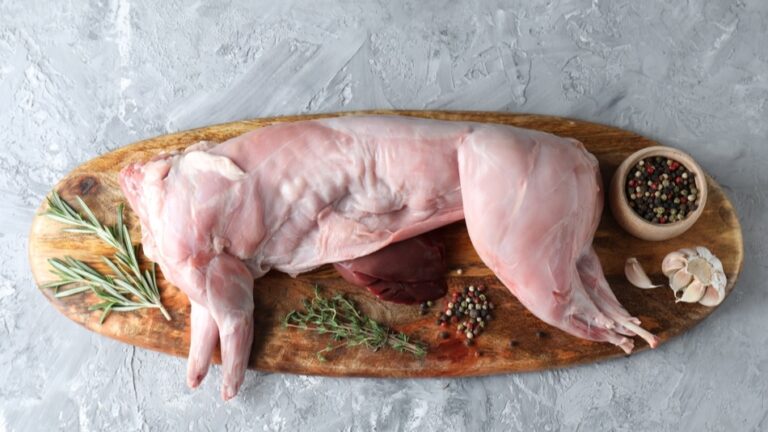 Frisch ausgenommenes Kaninchen, kunstvoll arrangiert mit Rosmarinzweigen, Thymian, Knoblauchzehen und bunten Pfefferkörnern – bereit für ein klassisches Gericht.