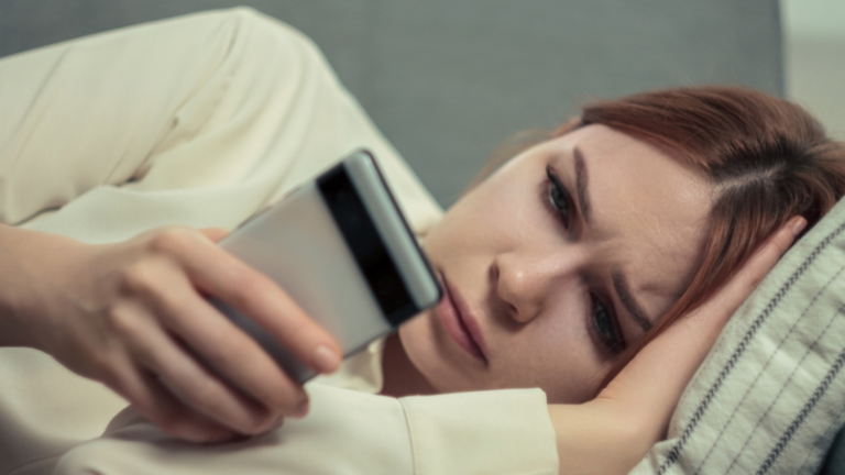 Das Bild zeigt eine junge Frau, die verzweifelt auf ihr Handy starrt.